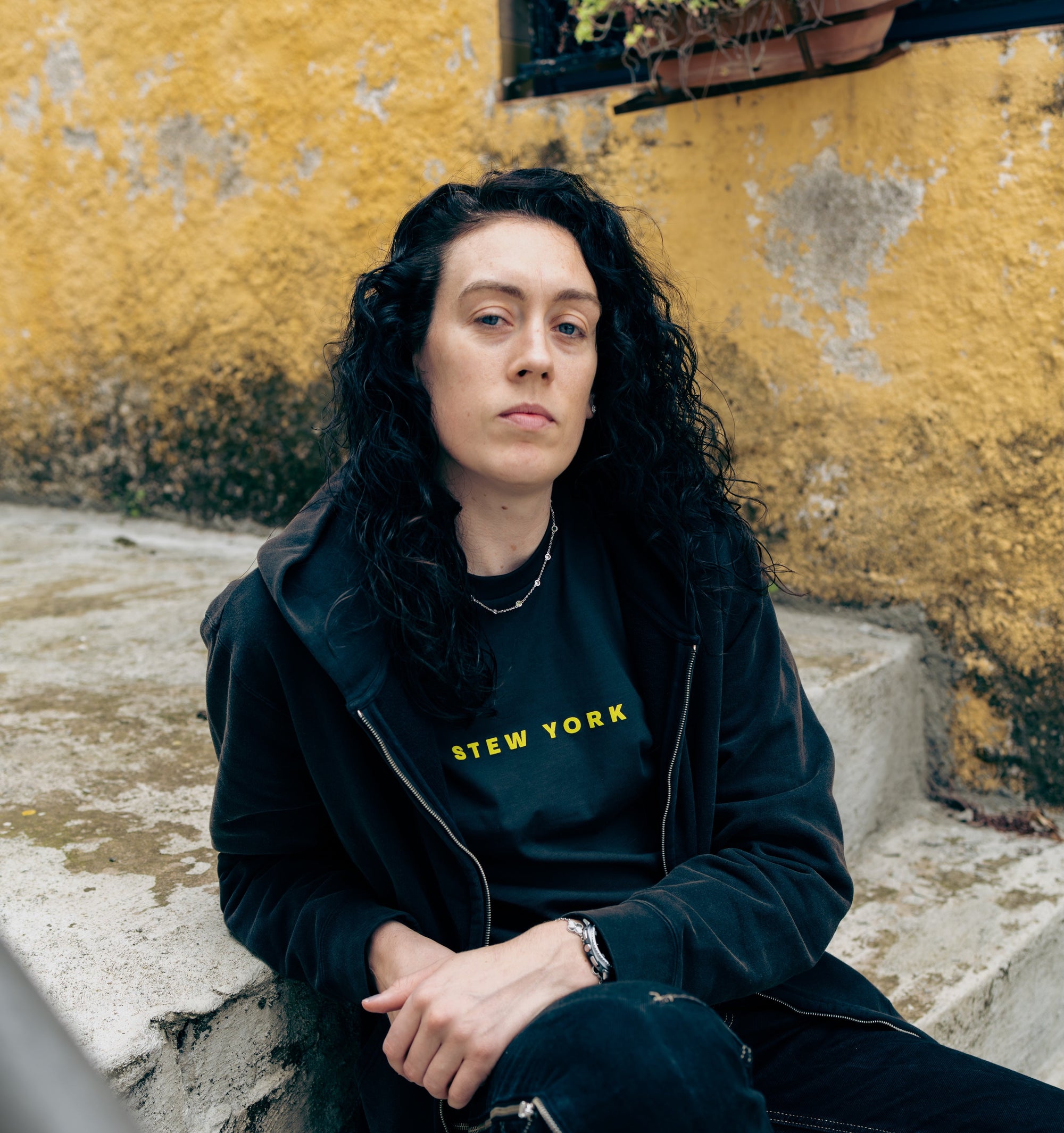 Stewie wearing Stew York Minute Tee sitting next to a yellow wall.