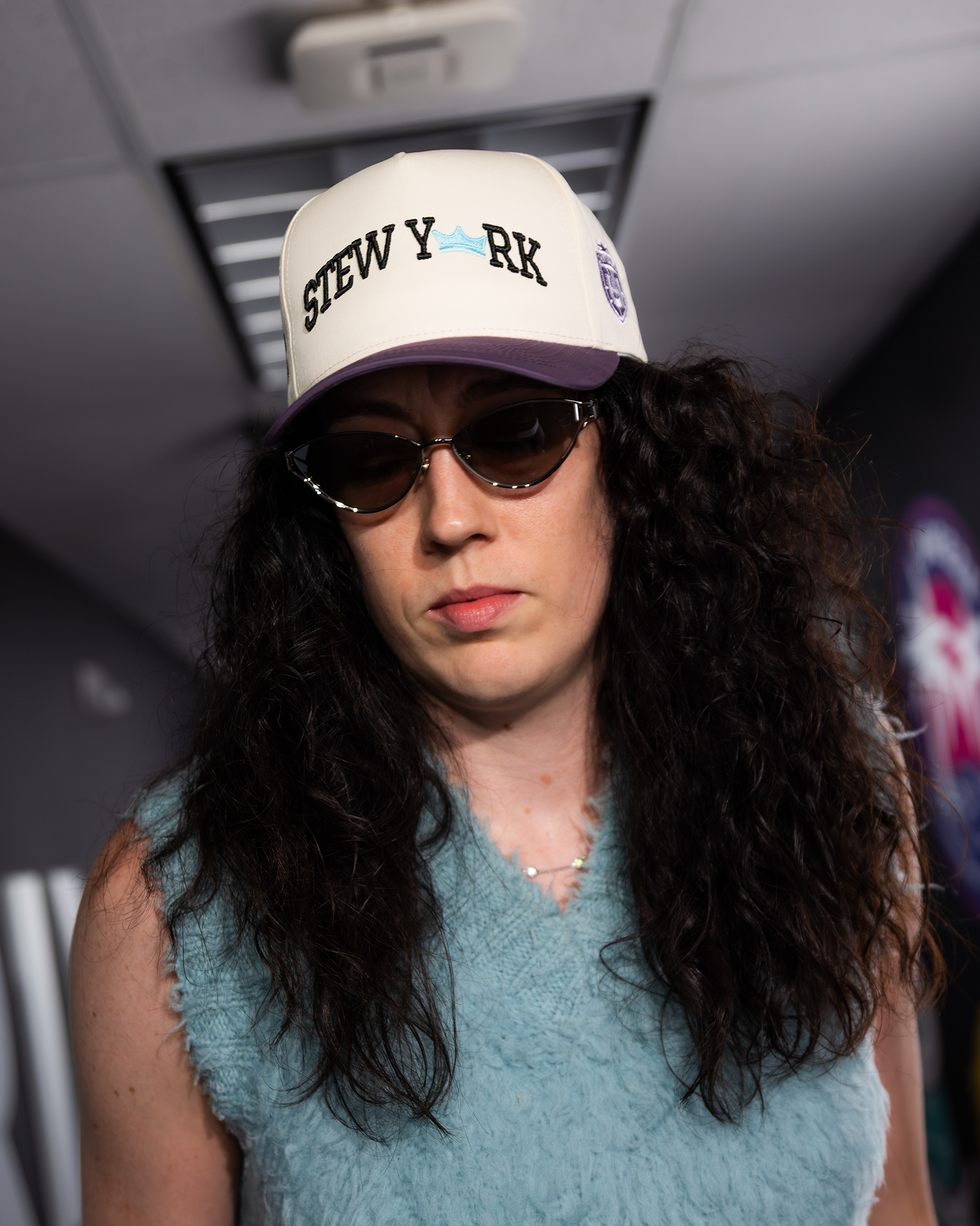 Person wearing a cap with text and sunglasses indoors