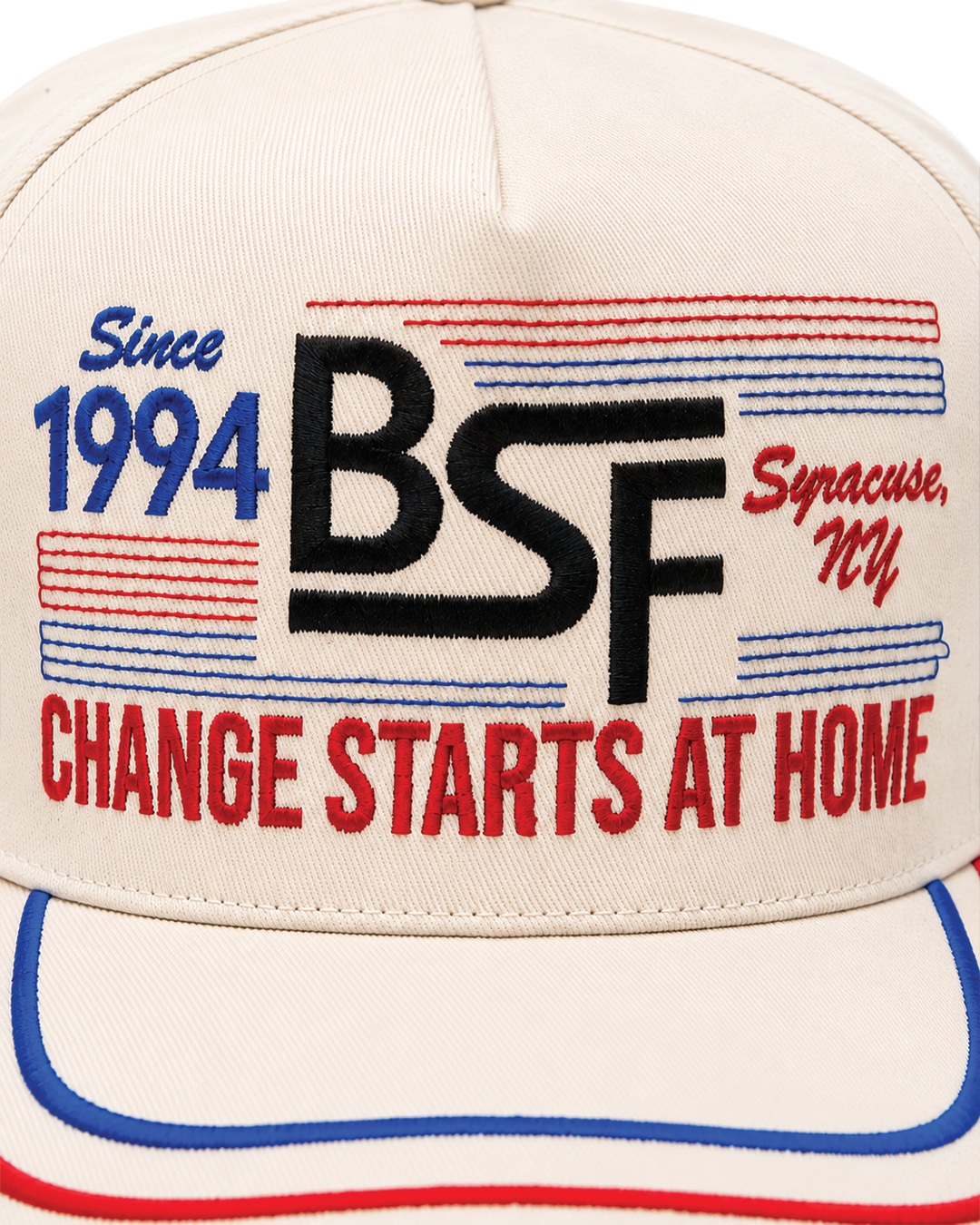 An off-white baseball cap featuring patriotic red and blue embroidered graphics and text on the front, including 'Since 1994', 'BSF', 'Syracuse, NY', and 'CHANGE STARTS AT HOME'.