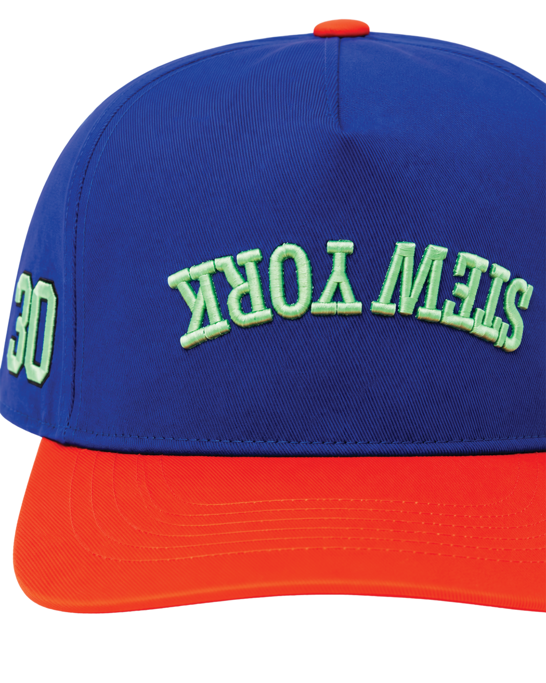 A close-up of a baseball cap featuring a royal blue crown with green embroidered 'STEW YORK' text on the front and a bright orange visor.