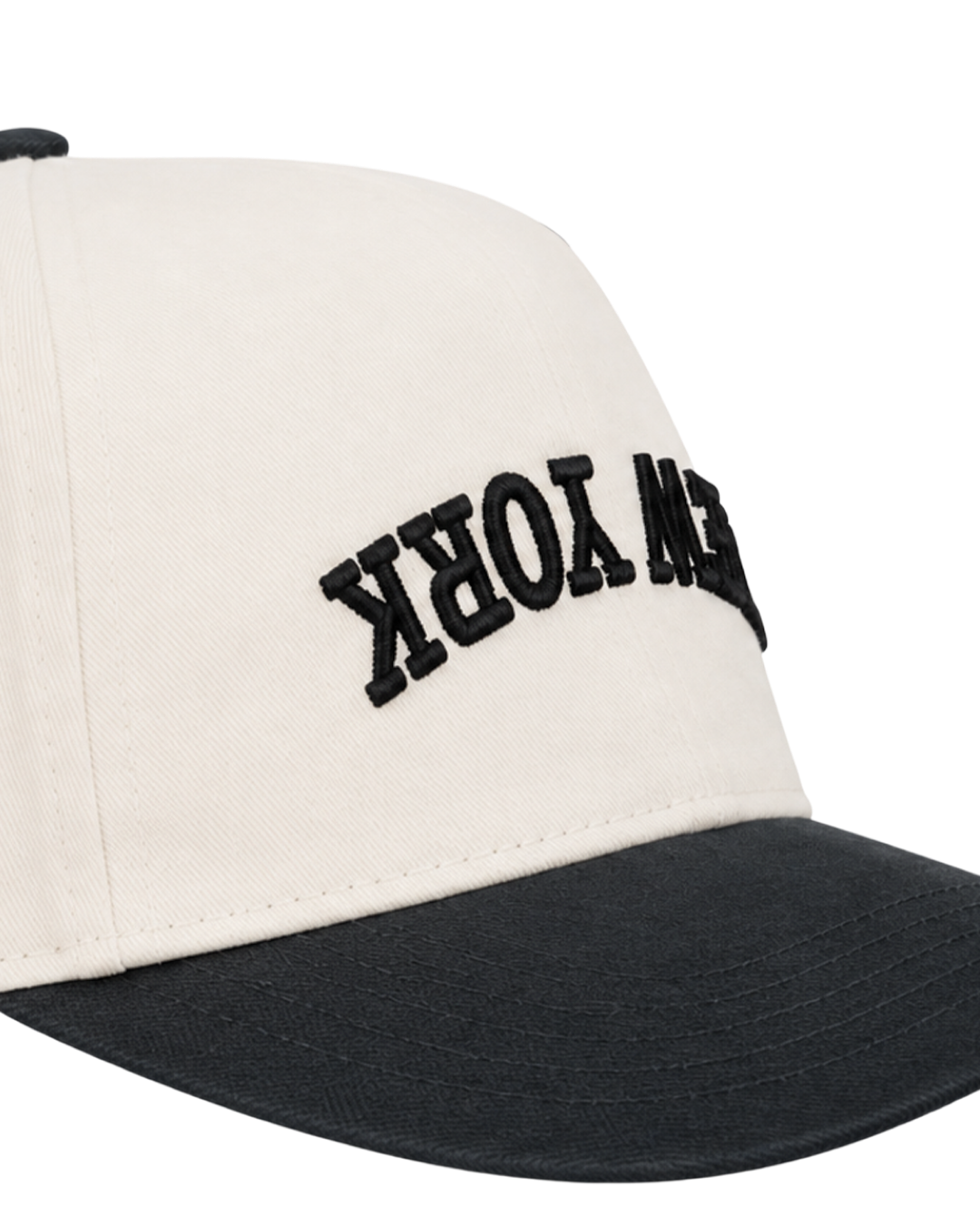 A close-up of a baseball cap with an off-white crown and a black curved brim. The front panel features the word 'STEW YORK' embroidered in black arched lettering.