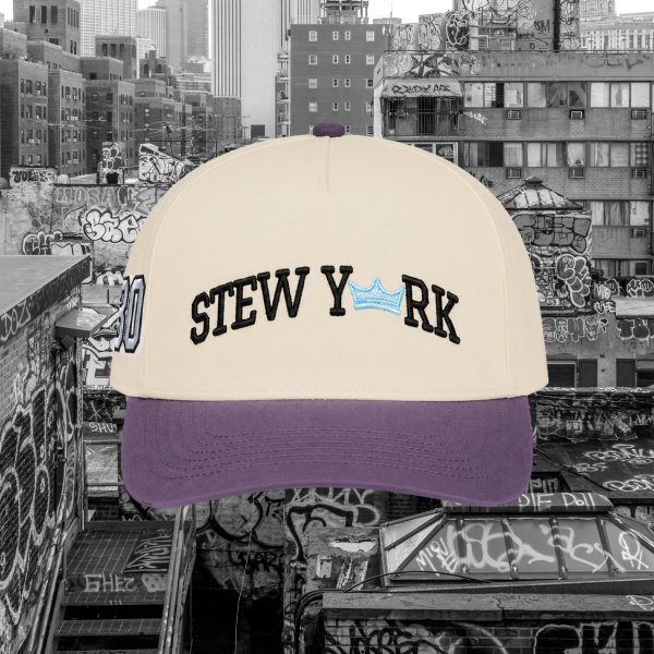A cream-colored baseball cap with a purple visor and black embroidered text reading 'STEW YORK' with a small blue crown graphic, shown against a black-and-white graffiti-covered city rooftop background.