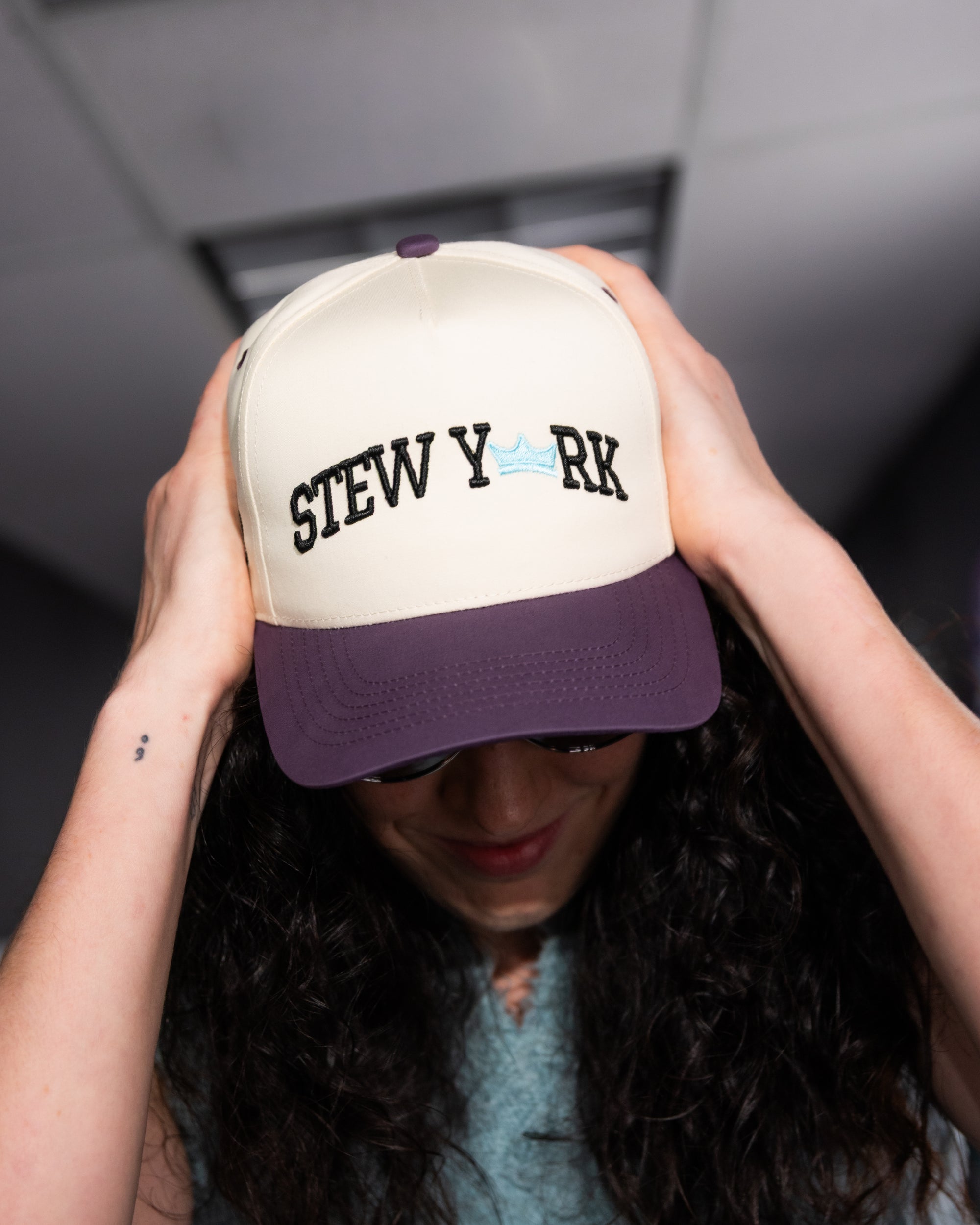 Person holding a cap with 'STEW Y'RK text against a neutral background